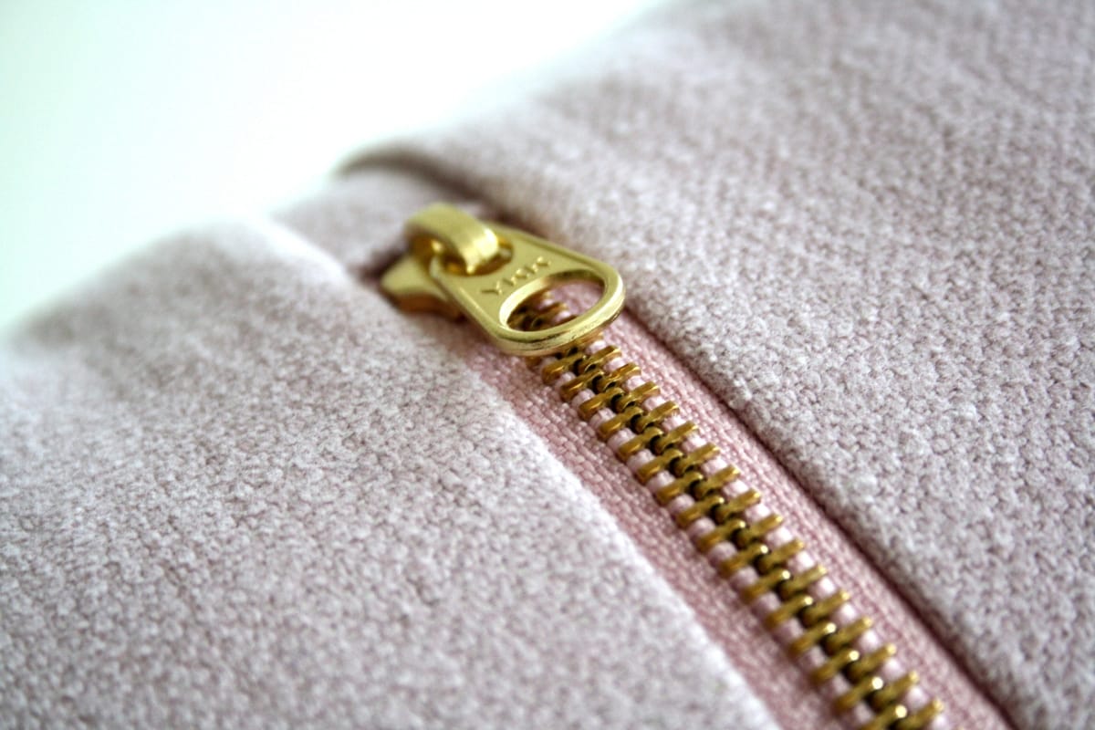 Close-up of a gold zipper on light pink textured fabric, partially unzipped—an elegant detail often seen on the best golf shorts.