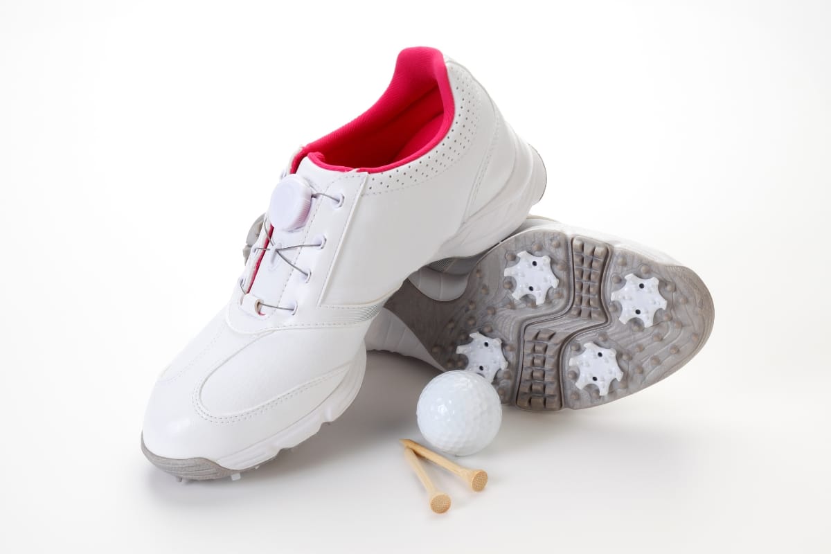 A pair of white golf shoes with pink lining, a golf ball, and two wooden tees on a white background—perfect for those seeking the best golf shoes for style and performance.