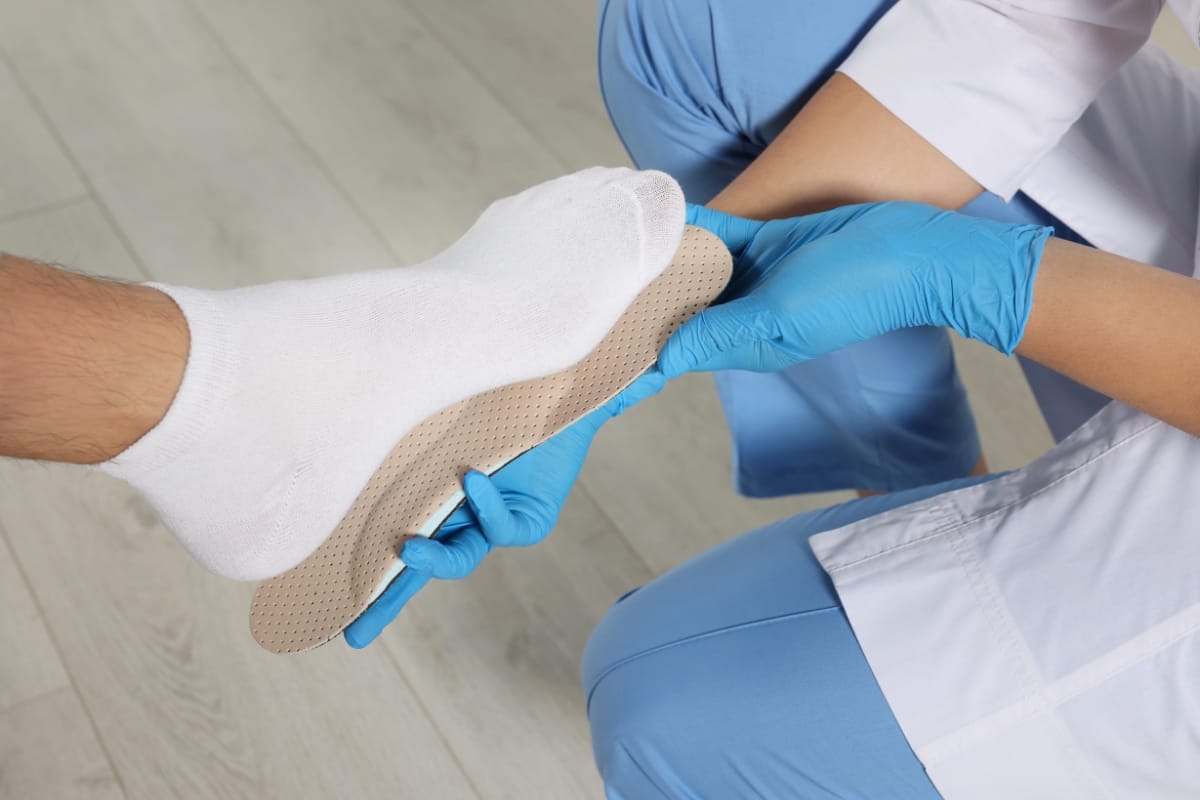 A healthcare professional in blue gloves fits a shoe insole to a person's sock-covered foot, ensuring maximum comfort often sought in the best golf shoes.