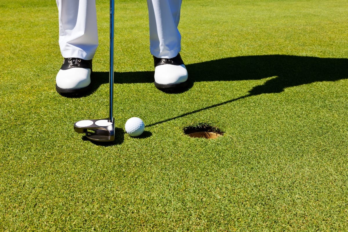 A golfer in golf socks stands on the green, preparing to putt a golf ball into the hole with a putter.