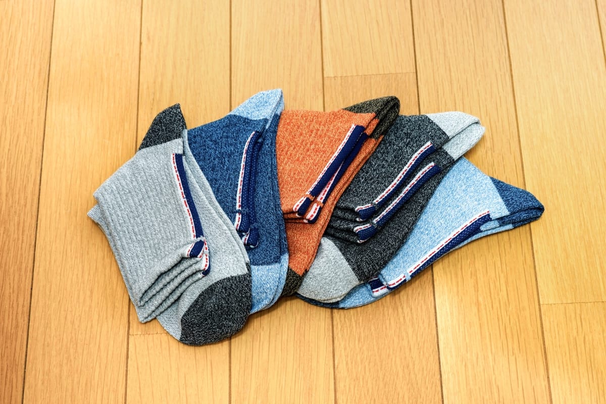 Five pairs of golf socks in various colors—gray, blue, orange, and black—are neatly arranged on a light wooden floor.