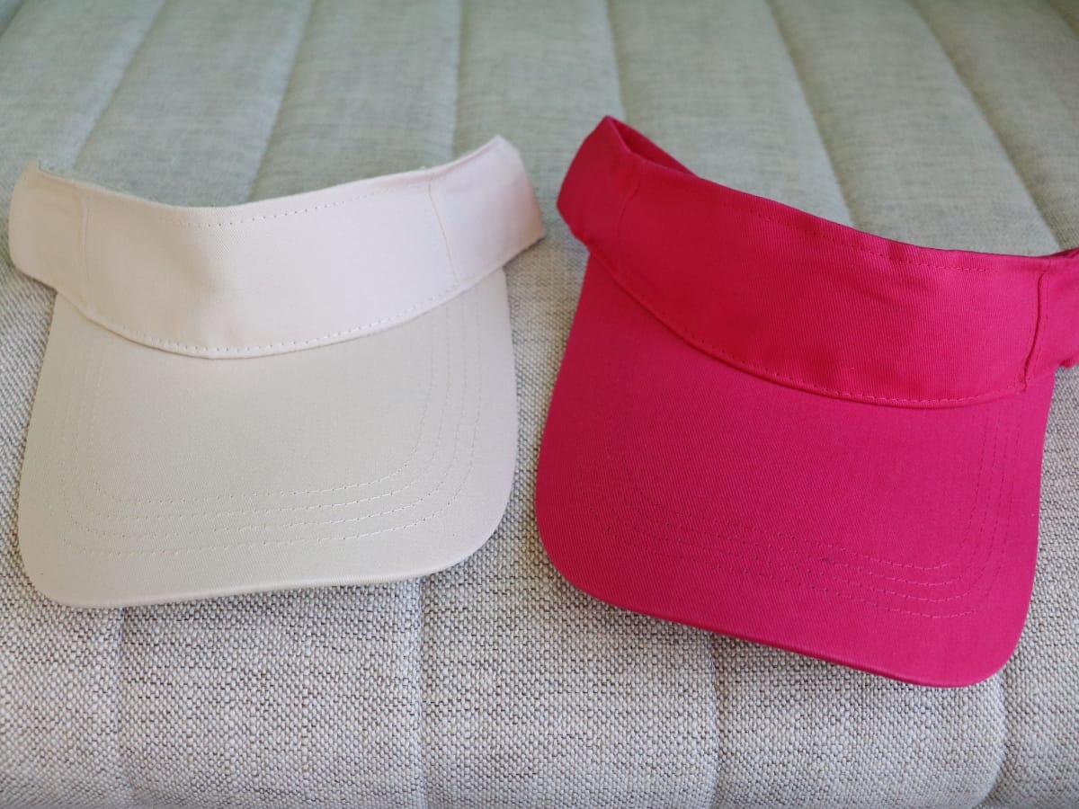 A beige visor hat and a pink visor hat, among the best golf visors, are placed side by side on a light gray textured surface.
