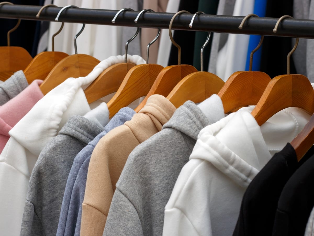 Several Best Golf Hoodies in neutral and pastel colors are neatly hung on wooden hangers on a clothing rack.