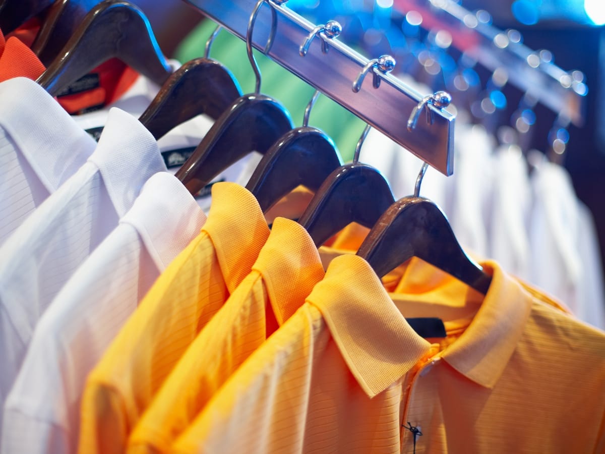 A row of collared shirts in white and yellow, perfect for layering tips for golf apparel, hang on wooden hangers on a metal rack.
