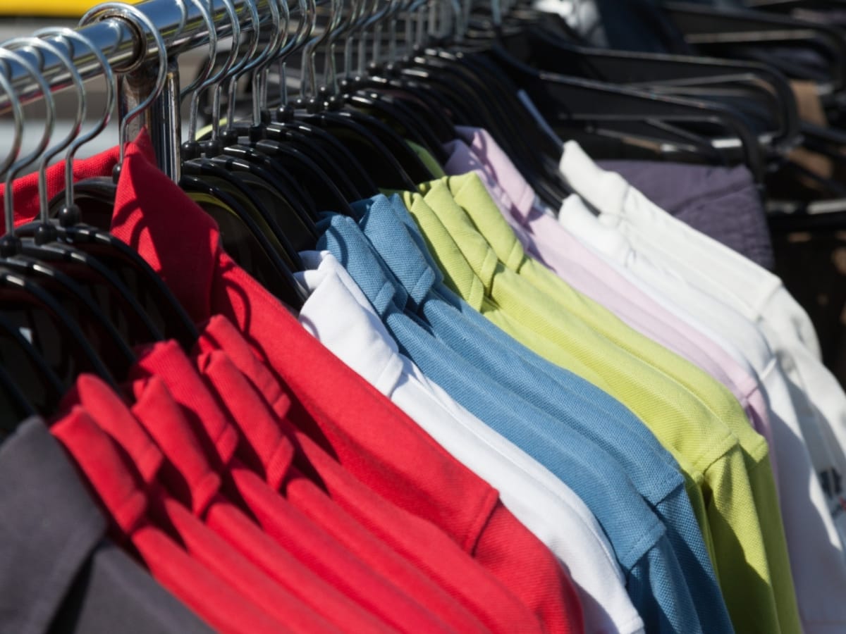 A row of colorful polo shirts—ideal for layering tips for golf apparel—hang neatly on black hangers, showcasing vibrant red, white, blue, green, and purple options on a clothing rack.
