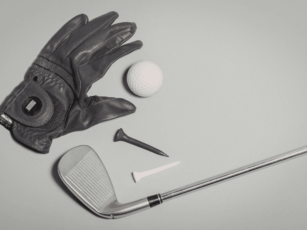 A golf glove, a golf ball, two tees, and an iron club are arranged on a gray surface, reflecting the latest Golf Apparel Trends.