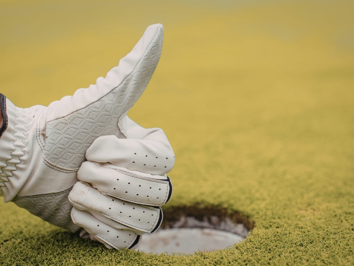 A gloved hand giving a thumbs up next to a golf hole on a green, showcasing reliable Rainy Weather Golf Gear.