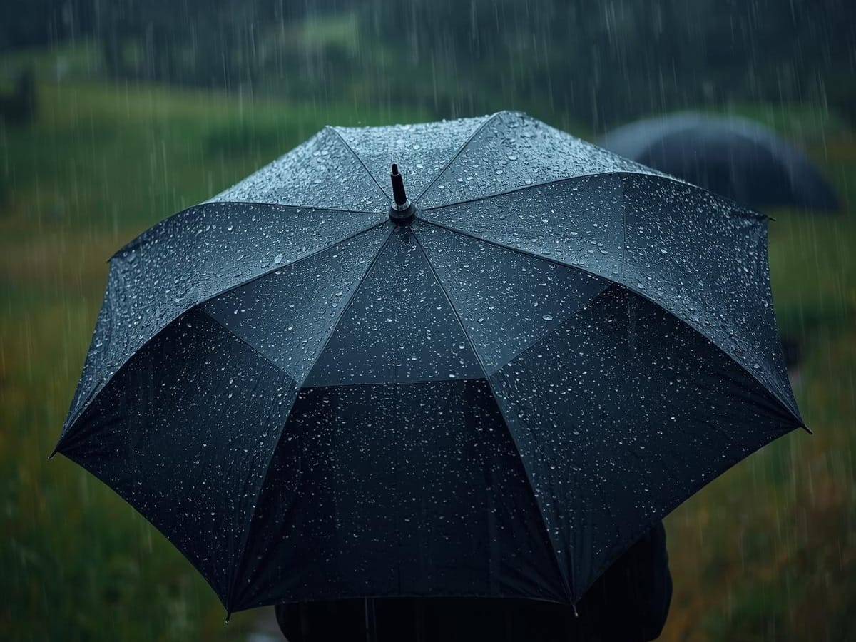 A black umbrella covered in rain droplets is held up outdoors during rainfall, with a blurred green landscape in the background—perfect for those seeking reliable rainy weather golf gear.