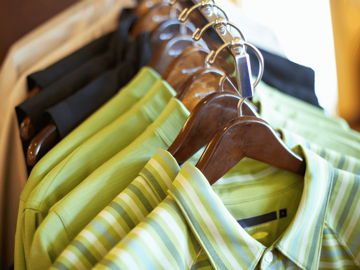 Several green collared shirts, crafted from moisture-wick fabric, are hanging on wooden hangers, with black and white shirts visible in the background.