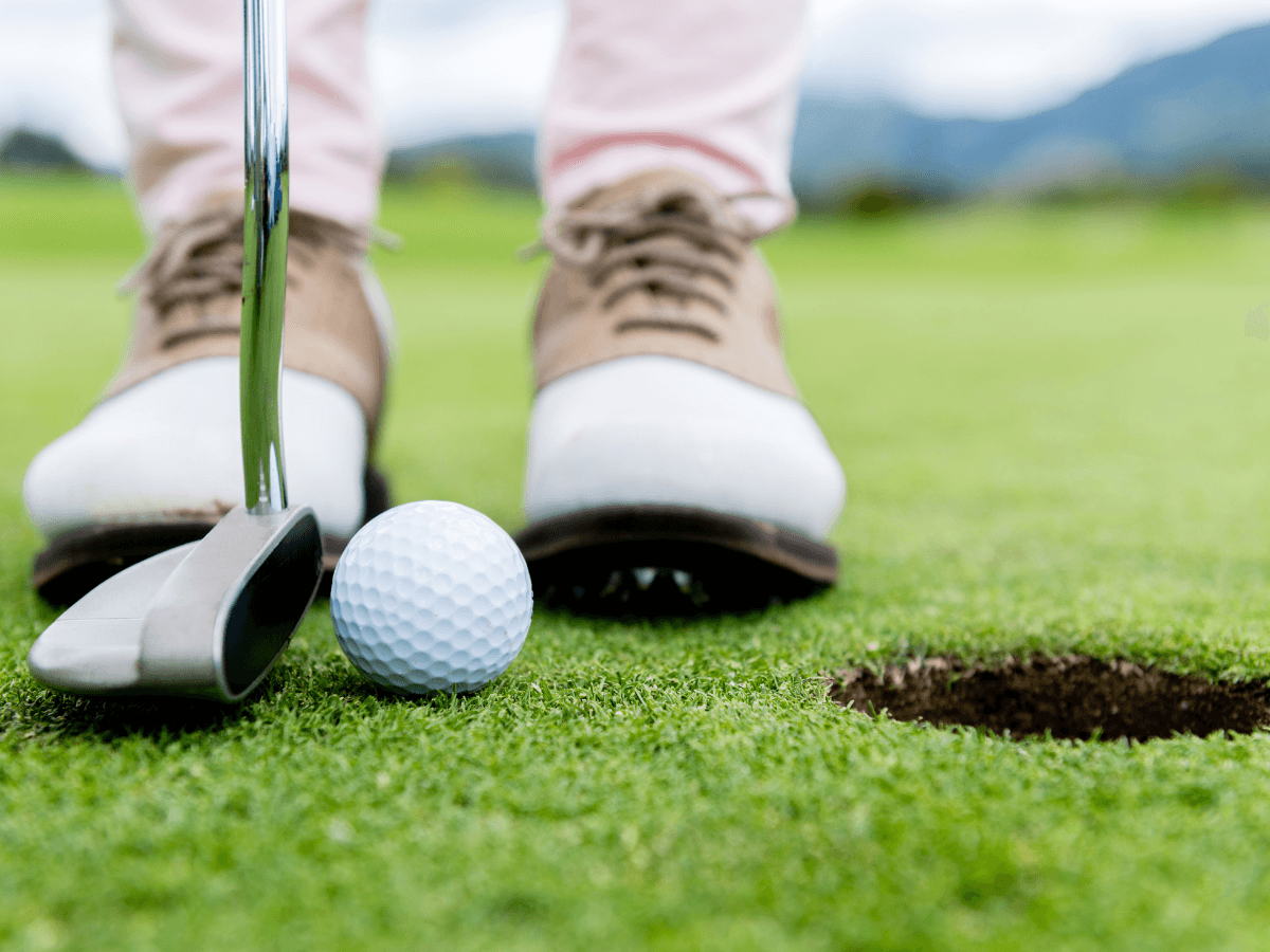 Close-up of a person putting a golf ball toward a hole on a green, with the putter and affordable golf shoes for men visible.