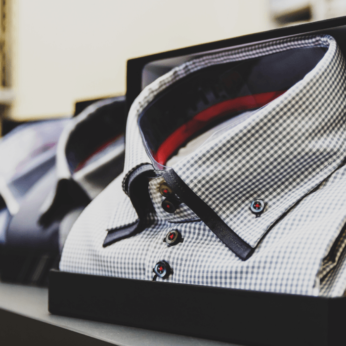 A neatly packaged checkered dress shirt with dark buttons is displayed on a shelf in a store, alongside other boxed shirts, reminiscent of the elegant presentation often seen with eco friendly golf apparel brands.