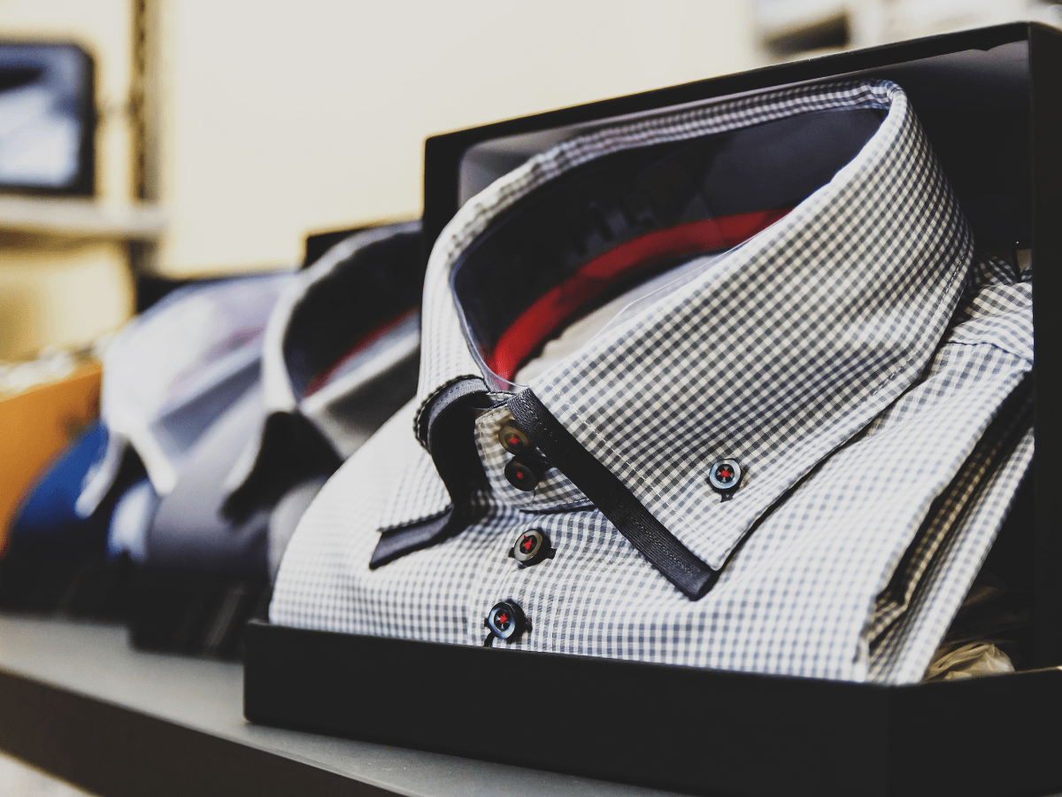 A neatly packaged checkered dress shirt with dark buttons is displayed on a shelf in a store, alongside other boxed shirts, reminiscent of the elegant presentation often seen with eco friendly golf apparel brands.